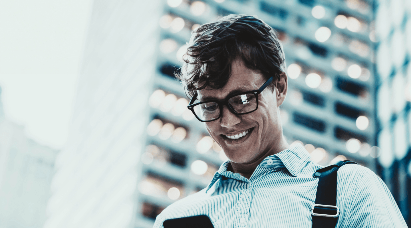 Core Banking - Foto de um homem de roupa social, sorrindo e olhando para o celular